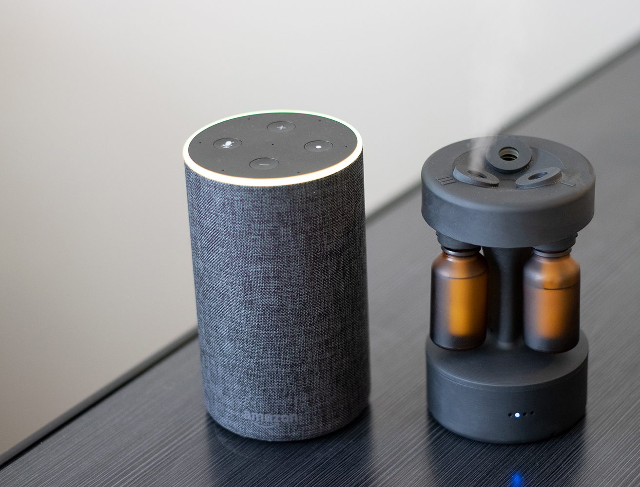 Curie diffuser beside an Amazon Echo on a dark table, blue LED visible, both roughly the same height.