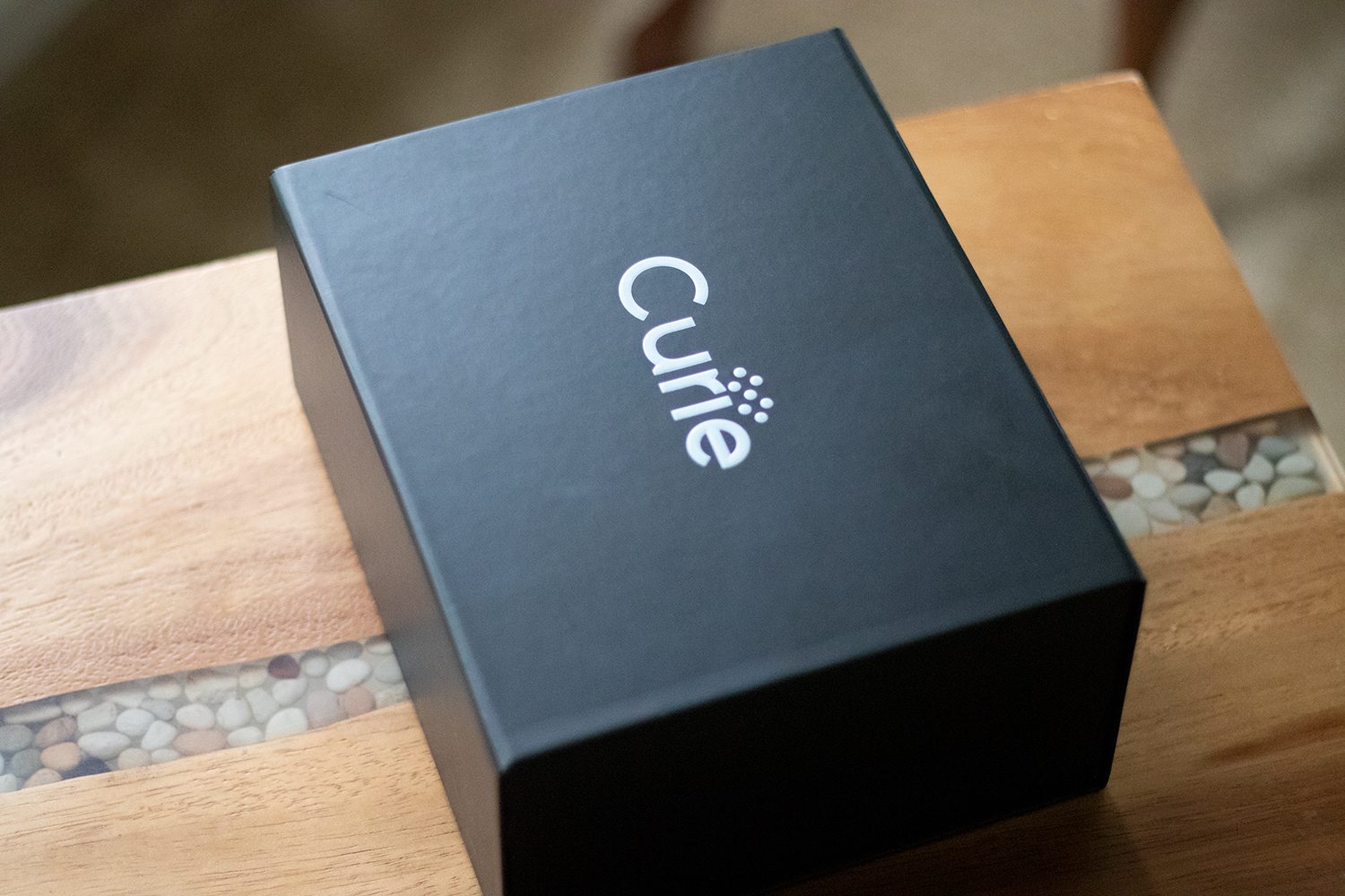 Curie retail packaging: a matte-black box with the Curie wordmark in white, on a wooden bench.